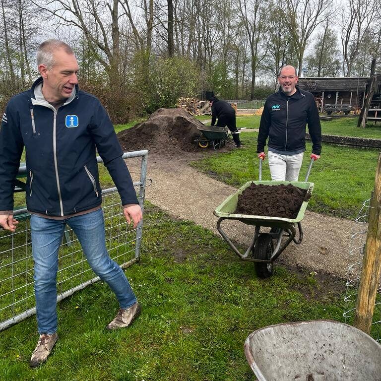 Twee medewerkers van New Nexus helpen met zand verplaatsen tijdens de New Nexus vrijwilligersdag