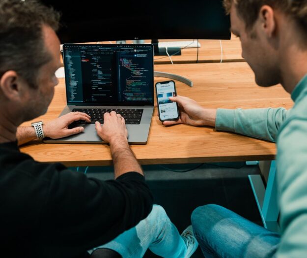 Twee programmeurs werken aan een app met de backend op een laptop en de frontend op een mobiele telefoon