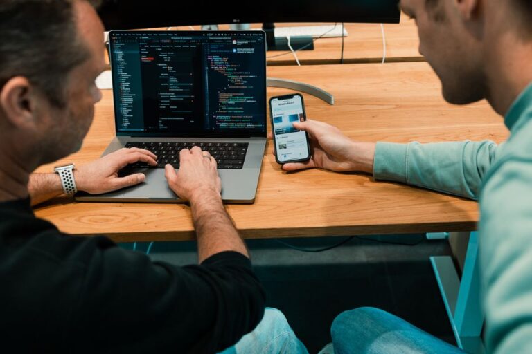 Twee programmeurs werken aan een app met de backend op een laptop en de frontend op een mobiele telefoon