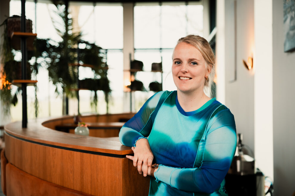 Annemijn van der Vaart leunt tegen hoge bank in bedrijfsrestaurant New Nexus tegen achtergrond van planten