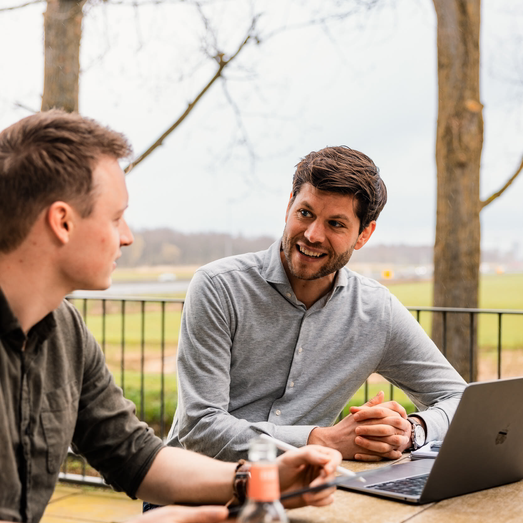 Alwin en Jan bij een laptop op tafel in gesprek op het dakterras met uitzicht op bomen en weiland