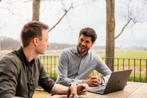 Alwin en Jan Galema in gesprek buiten MC Alwin en Jan bij een laptop op tafel in gesprek op het dakterras met uitzicht op bomen en weiland