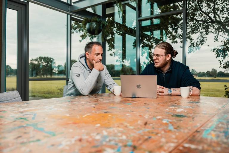 Jarno van der Woude en Tijs de Jonge in gesprek aan tafel bij laptop Jarno van der Woude en Tijs de Jonge in gesprek aan tafel bij laptop