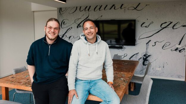 Header afbeelding Sociale Bouwmarkt Tijs de Jonge van New Nexus en Jarno van der Woude van Sociale Bouwmarkt zitten op tafel